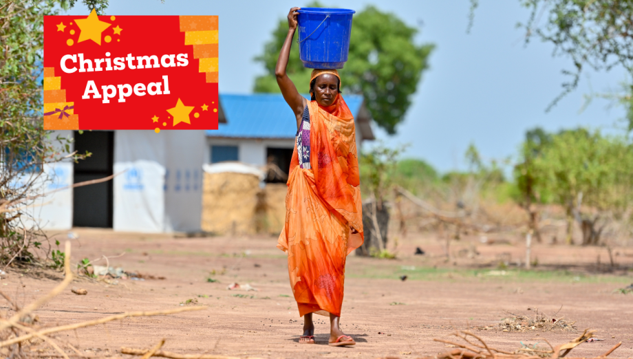 Shede, wearing orange and carrying a water bucket on her head.