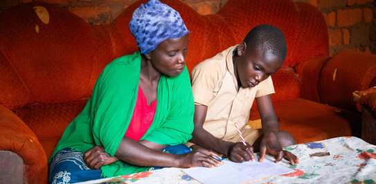 Aline Nibogora helping her son Vyukesenge Aubi with homework at their home in Makamba Province, Burundi.